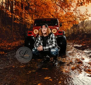 A man sitting in the mud with his jeep behind him.
