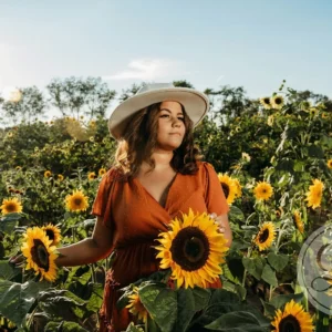 A woman in a field of sunflowers wearing an orange dress and hat.