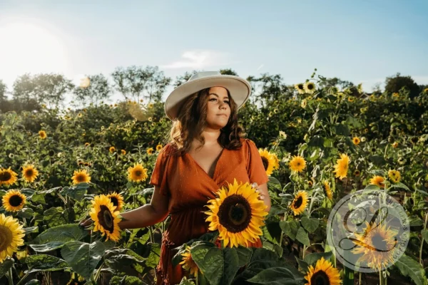 A woman in a field of sunflowers wearing an orange dress and hat.