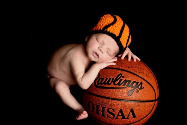 A baby is sleeping on top of a basketball.