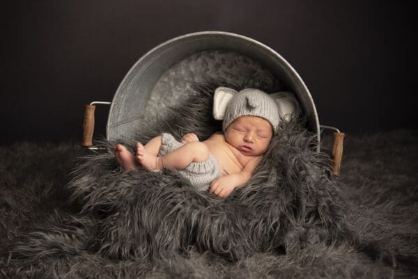 A baby is wearing a hat and sitting in a bucket