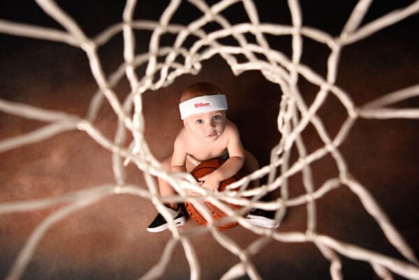 A baby is sitting in the middle of a basketball net.