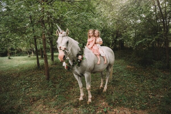 Two girls riding on the back of a white unicorn.