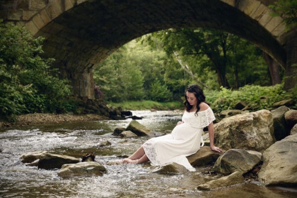 A woman in white dress sitting on rocks near water.